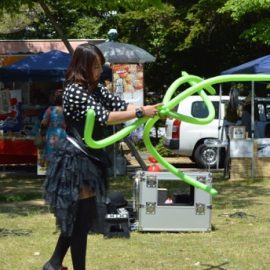 芝生広場でのイベントでお客様の目の前でバルーンを作る女性パフォーマー