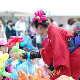 観客のお子様に花のバルーンをプレゼントするバルーンパフォーマー