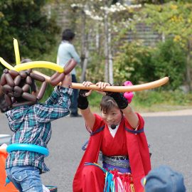 ショー中にバルーンで作った剣で男の子と戦う仕草をするバルーンパフォーマー