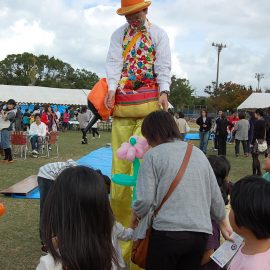 小さな女の子に花のバルーンアートをプレゼントするスティルトパフォーマー