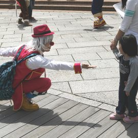 路上で通行人に対してパフォーマンスをする男性クラウン（ピエロ）